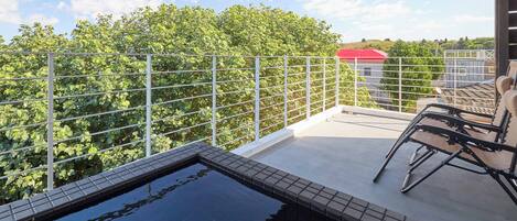 A rooftop terrace with a swimming pool, a metal railing, and a view of trees and buildings.
