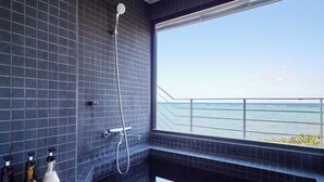 Ein Badezimmer mit dunkel gefliesten Wänden, einer Dusche und einem Fenster mit Blick auf ein Gewässer.