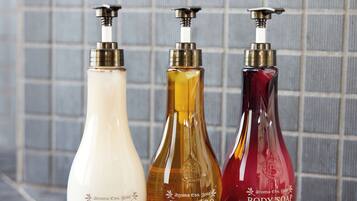 Tres botellas de jabón de cuerpo con dosificadores, etiquetadas 'aroma Ess. Gold', frente a una pared de azulejos.
