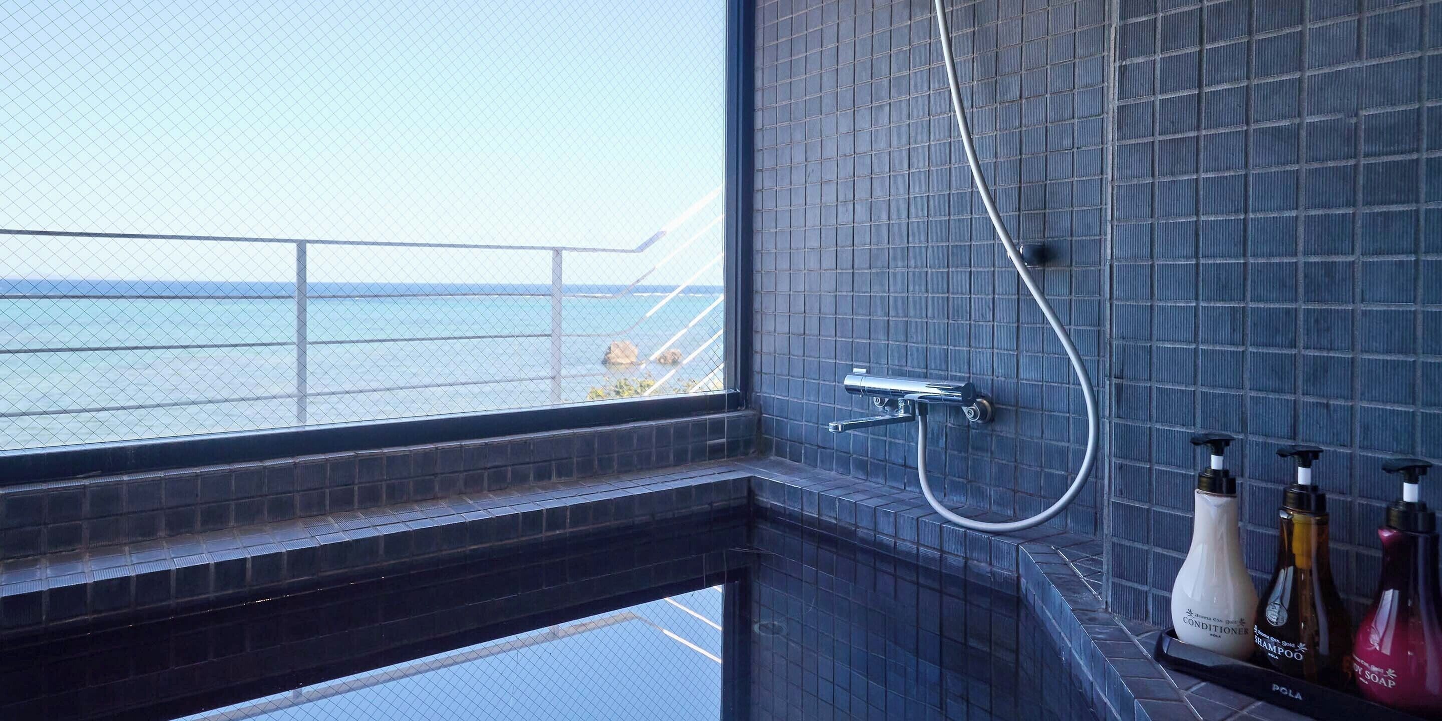 A bathroom with a view of the sea, a shower, and a shelf with toiletries.