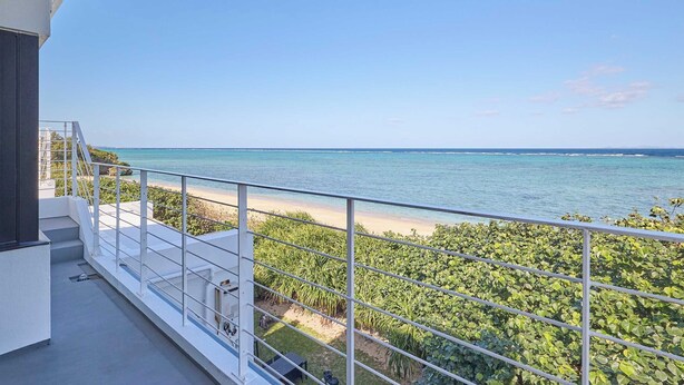 Ein Balkon mit Blick auf das Meer und den Strand, mit Metallgeländer und Pflanzen.