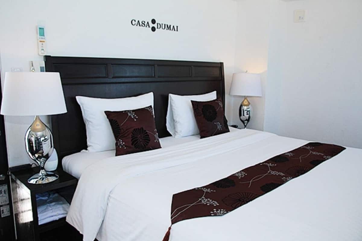 Ein Hotelzimmer mit einem Bett, zwei Nachttischen, zwei Lampen, einem kleinen Tisch und einem an der Wand montierten Thermostat.