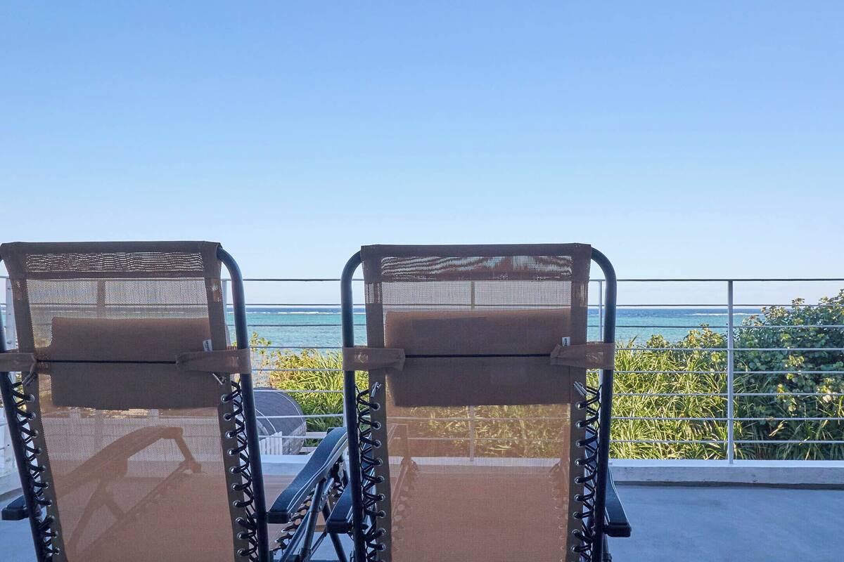 Zwei Liegestühle mit Netzrücklehnen blicken auf einen Balkon mit Blick auf ein Gewässer.