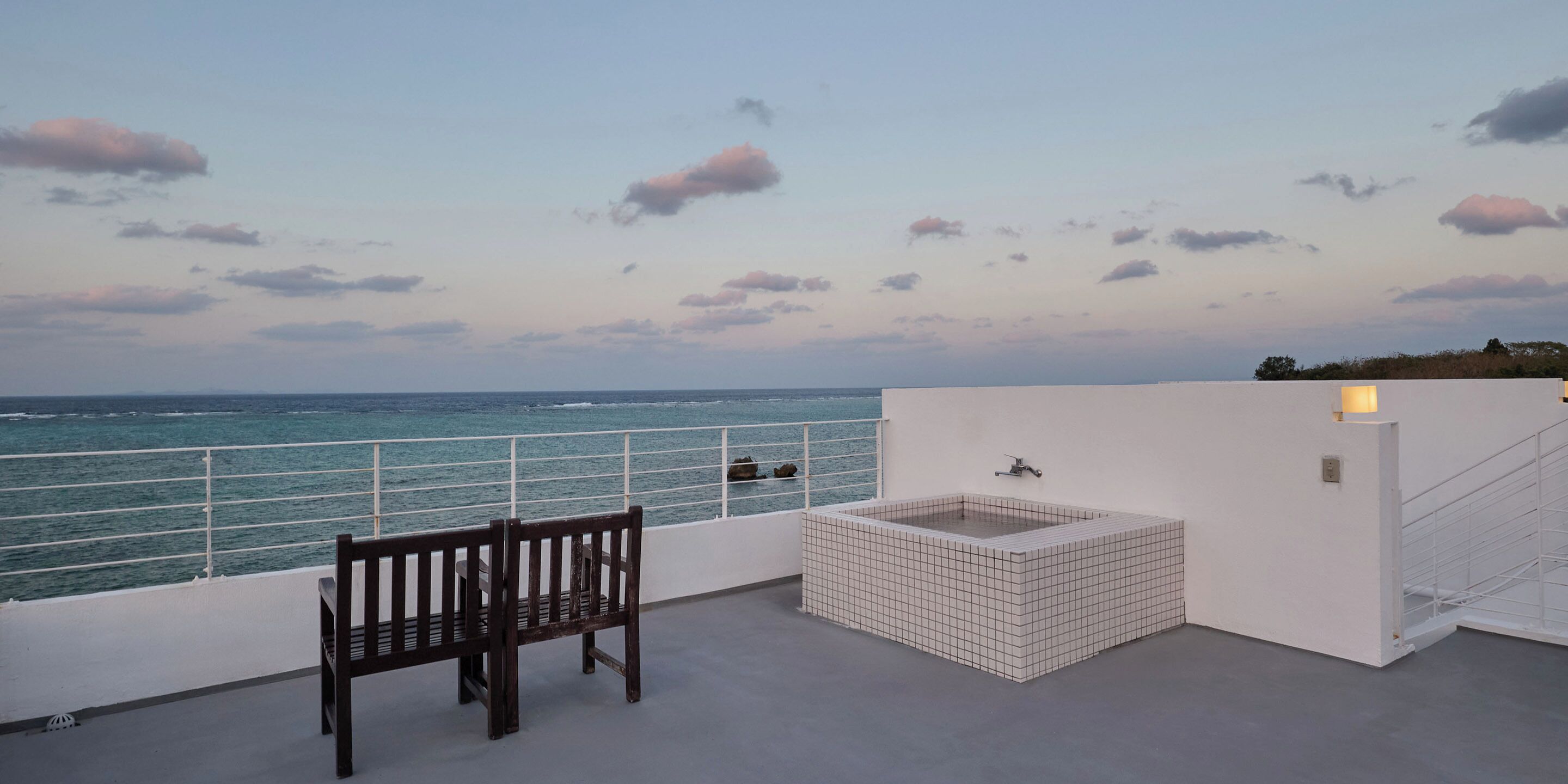 Uma varanda com um banco e uma pequena banheira de hidromassagem com azulejos, com vista para o mar.