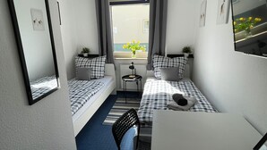 Habitación de hotel compacta con dos camas individuales, una mesita, una silla y un televisor.