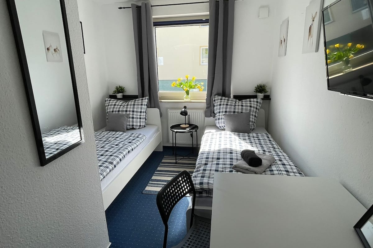 Habitación de hotel compacta con dos camas individuales, una mesita, una silla y un televisor.