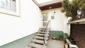 Una escalera estrecha que lleva a una puerta, una parrilla pequeña al aire libre y una planta verde cerca de la puerta.