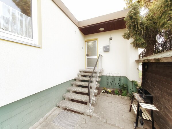 A narrow stairway leading to a door, a small outdoor grill, and a green plant by the door. - Gästezimmer Kreuzheide (Wolfsburg)