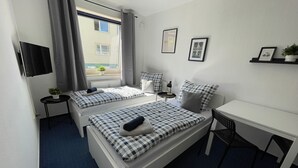 Una habitación moderna y funcional con dos camas, un escritorio y una pequeña mesa.