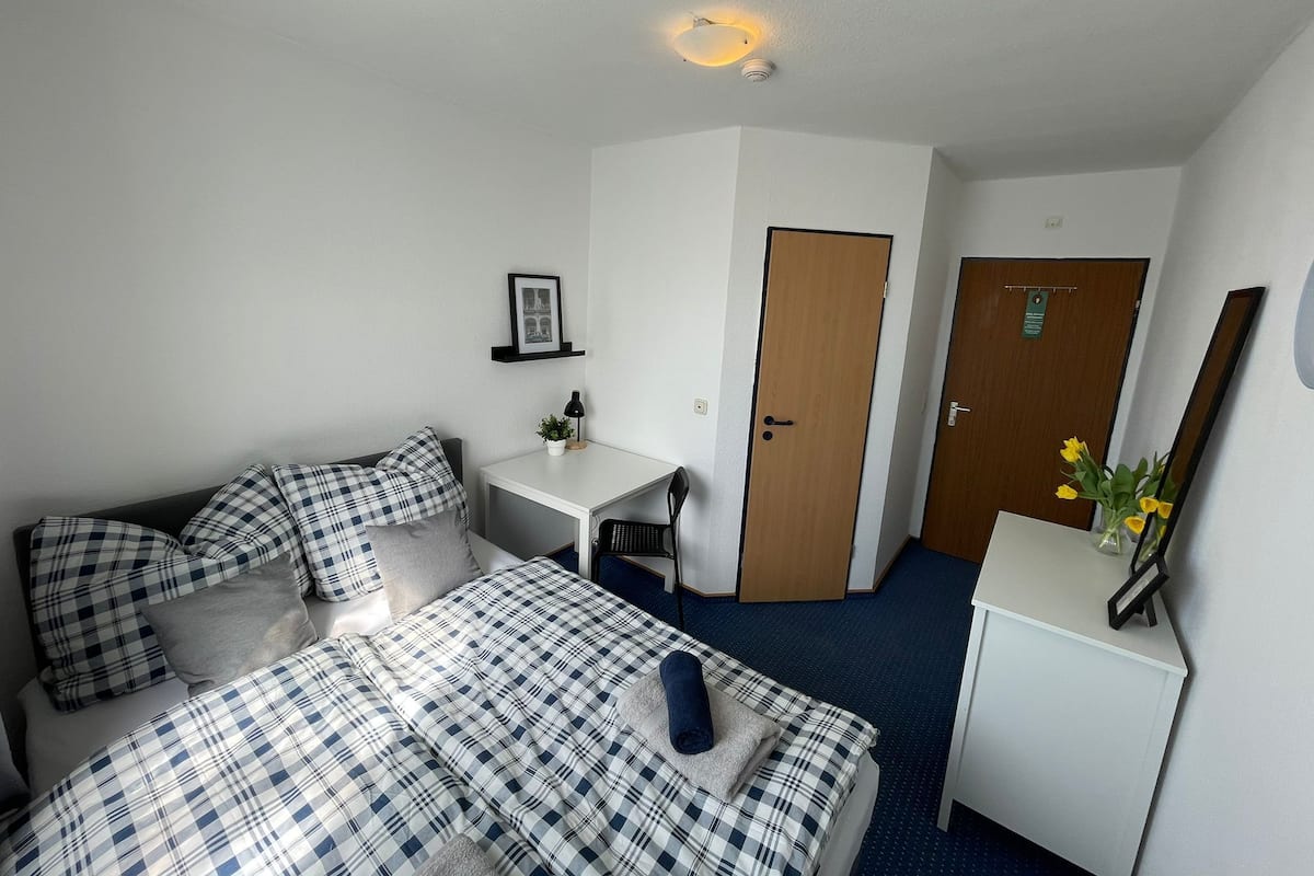 Habitación de hotel con cama, escritorio, silla, mesita, puerta y espejo.