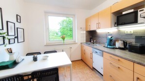 Una cocina moderna con armarios de madera, encimera blanca, microondas integrado y ventana con vistas a zonas verdes.