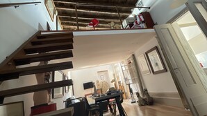 A spacious room with a wooden ceiling, a staircase, and a dining area with a table and chairs. - Piraeus House With Sea View and Free Parking (Piraeus)