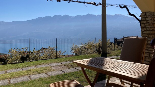 Eine Terrasse mit Tisch und Stühlen mit Blick auf eine Berglandschaft und einen See.