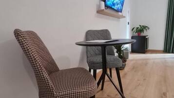Una sala moderna con una butaca estampada de piedritas, una mesita redonda pequeña, un televisor de pantalla plana montado en la pared y una planta en maceta.