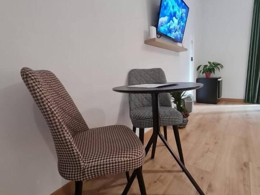 Una sala moderna con una butaca estampada de piedritas, una mesita redonda pequeña, un televisor de pantalla plana montado en la pared y una planta en maceta.