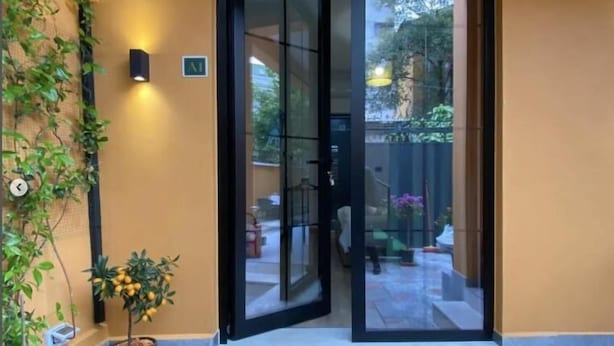 Entrada de hotel con puerta de cristal, un pequeño espacio de estar al aire libre y plantas en macetas.