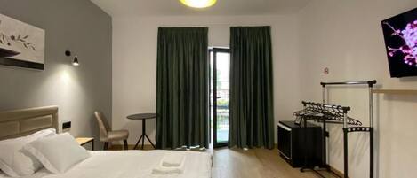 Una habitación de hotel con cama, escritorio, silla, televisión y ventana con cortinas.