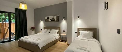 A modern hotel room with two beds, a large window with a view, and a ceiling light fixture.
