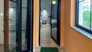 Un pasillo con puertas de cristal que dan a un dormitorio, una mesita con lámpara y una ventana con vistas a zonas verdes.