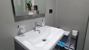 Un baño con un lavamanos blanco, un espejo, una toalla y un estante con artículos de aseo.