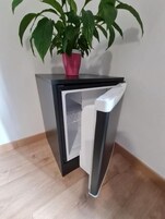 A small, modern refrigerator with a white interior, placed on a wooden floor against a plain wall.