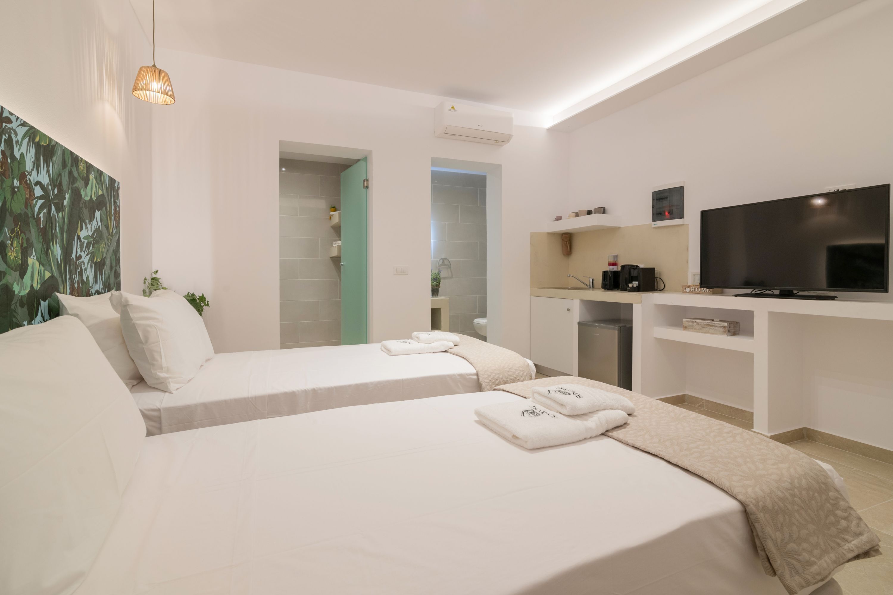 A hotel room with two beds, a TV, a desk, and a bathroom visible through an open door.