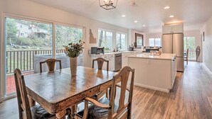 A spacious kitchen with a central island, large windows, and a dining area with wooden chairs.