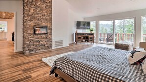 A spacious bedroom with a large bed, a stone fireplace, a television, and a balcony with a view of the outdoors.