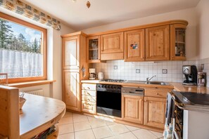 A kitchen with wooden cabinets, a stove, a dishwasher, and a window with a view of trees. - Mendelhaus Holiday Home with Mountain View, Private Garden and Wi-Fi (Mendel)