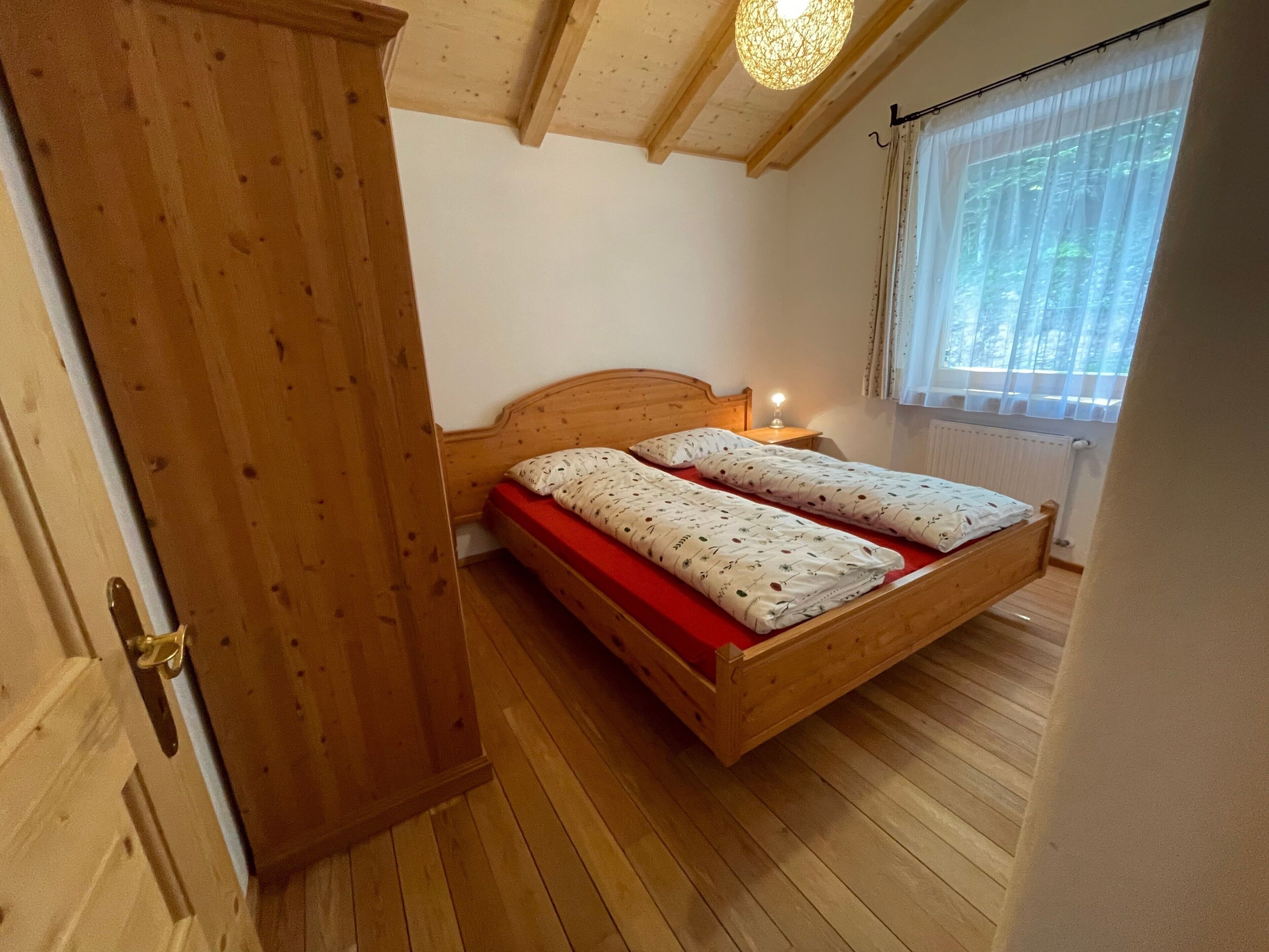 Una cama de madera con colchón rojo en una habitación con suelo de madera y techo inclinado.