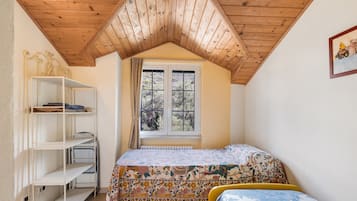 Ein Schlafzimmer mit schrägen Wänden, einem Fenster mit Ausblick, einem Bett mit Blumenmuster-Decke und einer weißen Regaleinrichtung.