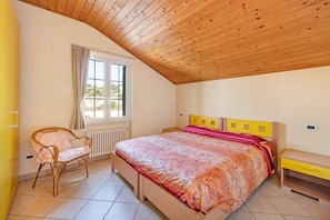 Ein Schlafzimmer mit Holzboden, einem Bett mit gemustertem Überwurf, einem Nachttisch, einem Stuhl und einem Fenster mit Vorhängen.