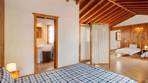 A bedroom with a wooden ceiling, a bed with a checkered bedspread, a bedside table with a lamp, and a bathroom visible through an open door. - Vacation Home 'Mirador de la Abuela' with Sea View, 2 Terraces & Wi-Fi (Gáldar)