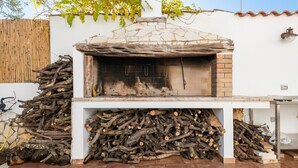 Een buitenoven van baksteen met een stenen dak, omringd door een stapel hout.