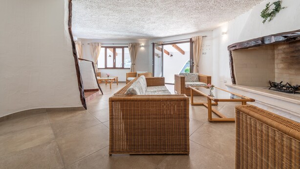Een ruime woonkamer met rieten meubels, een open haard en grote ramen.