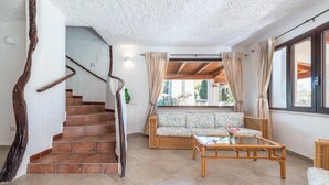 Een woonkamer met een trap, rieten meubels en een groot raam.