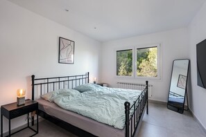 A bedroom with a bed, bedside table, nightstand, window, radiator, and a mirror.