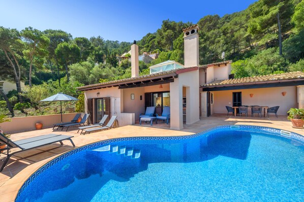 A villa with a swimming pool, outdoor seating, and a view of the surrounding forest.