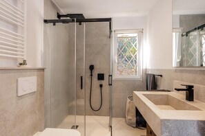 A modern bathroom with a glass-enclosed shower, a large window, and a stone sink.