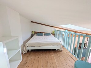 Ein Schlafzimmer mit Holzboden, einem weißen Bett und einem Balkon mit blauer Brüstung.