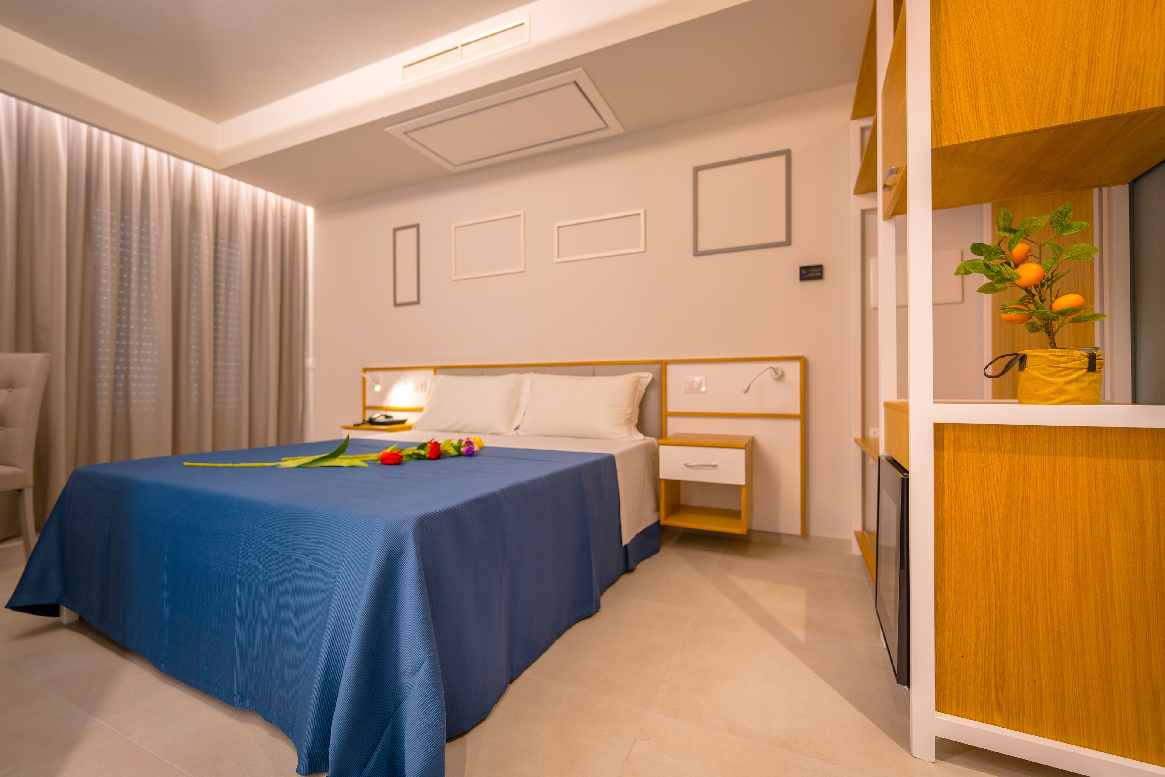 A neatly arranged hotel room with a bed, bedside table, and a small wooden cabinet with a plant.