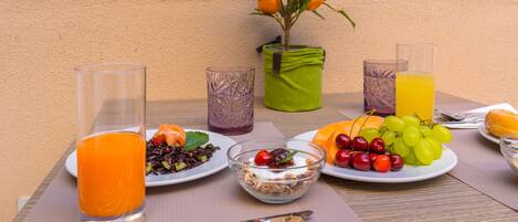 A table set with breakfast items including orange juice, grapes, and a salad, with a brick wall and window in the background.