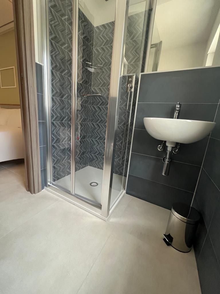 Une salle de bain avec une douche à parois de verre, un lavabo blanc et des murs recouverts de carreaux foncés.