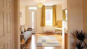 A cozy living room with a sofa, a chair, a patterned rug, and a window with curtains. - 2BR Stylish Norwich Stay Near Cathedral | Parking (Norwich)