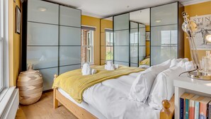 Un dormitorio moderno con una cama grande, una mesita de noche con libros, un espejo y vistas al exterior.