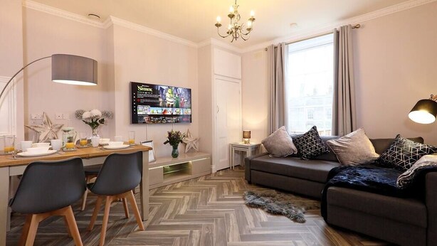 Ett modernt vardagsrum med en soffa, en tv och en matplats med stolar och ett bord.