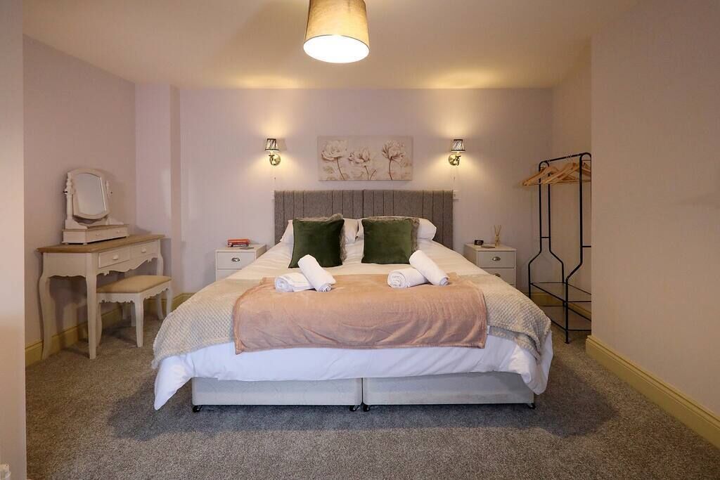Ein ordentlich eingerichtetes Schlafzimmer mit einem Bett, Nachttischen, einem Schreibtisch und einer Kleiderstange.