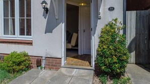A house with a white exterior, a number '58' sign, a small front garden, and a door leading to an interior with a chair visible.