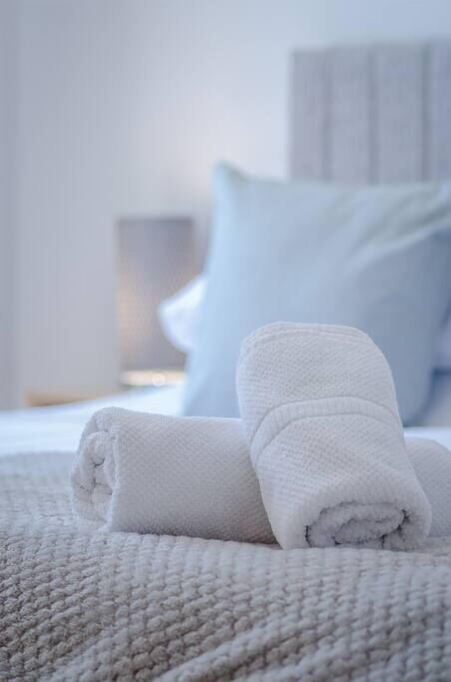 Un letto rifatto con lenzuola e cuscini bianchi, una coperta con trama e una testiera in legno.