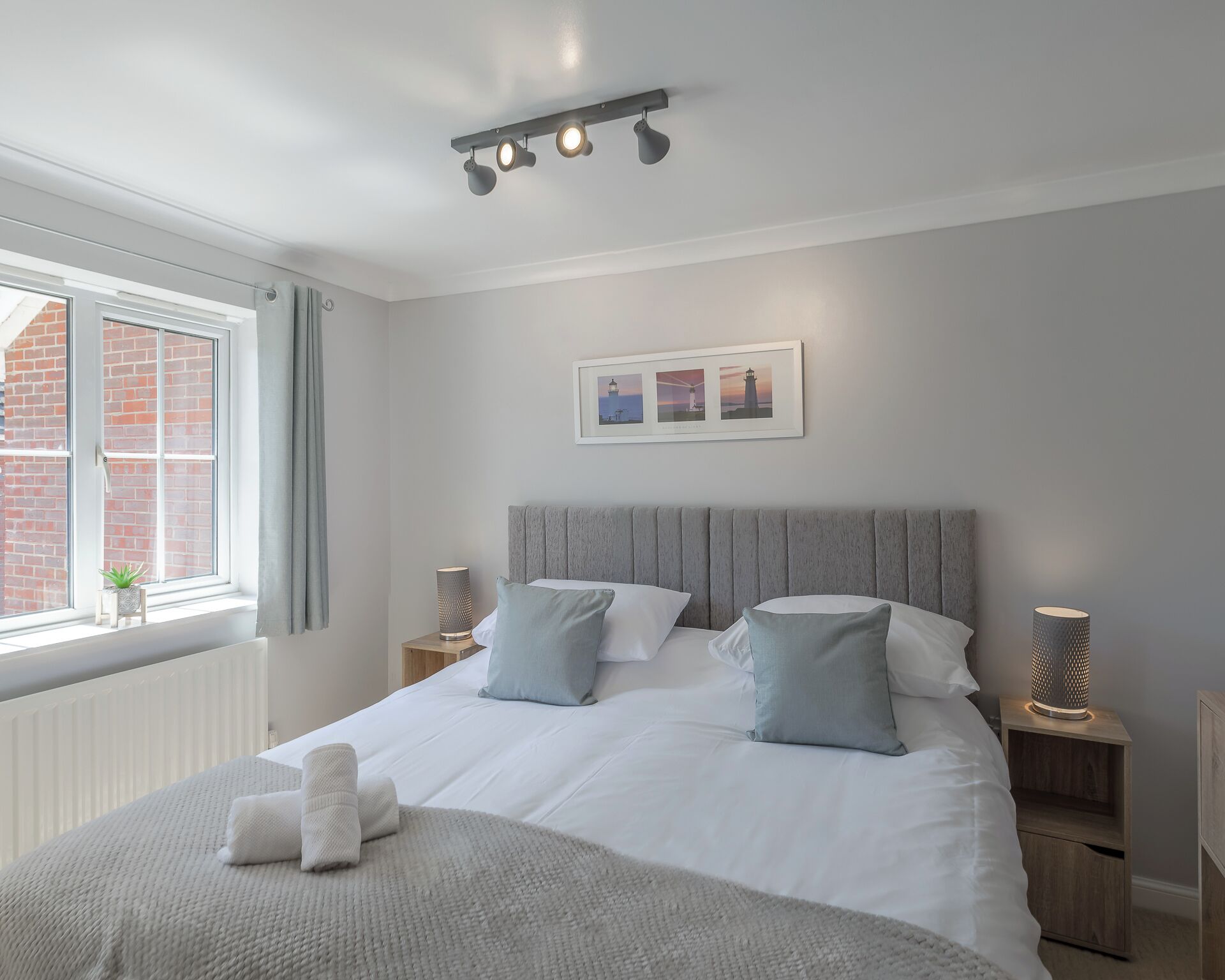 Una camera da letto con un letto, comodini, una finestra con tende, un quadro appeso al muro e un lampadario.